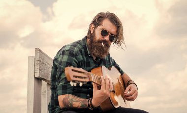 Müzik konsepti. Bıyıklı vahşi yakışıklı adam gitar çalıyor. Olgun müzisyen ve şarkıcı. Sıradan stil gitarist. Modern görünümlü sakallı, akustik gitarlı hippi. Düşürenleri yener.