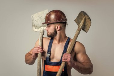 Yapı ve inşaat. Kürekli seksi adam. Profesyonel inşaatçı ya da tamirci. İnşaat mühendisi. Güçlü vücutlu kaslı bir mimar. Adam işçi üniforması giyiyor. Miğferli atletizm ustası.