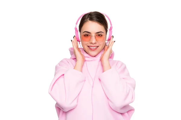 幸せな女性学生でカジュアルピンクパーカーと眼鏡リッスンオーディオコースでヘッドフォンで隔離された白 — ストック写真