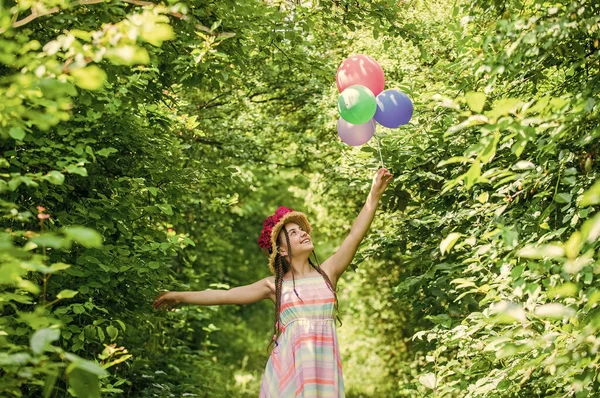 Hasır şapkalı mutlu bir kız. Yazın gül çiçekleri içinde. Parti balonları ve hayalleri var..
