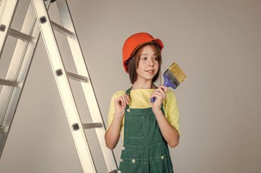 Bina ve inşaat. Çocuk mimar. Mühendis fırça kullanıyor. İşçi çocuk güvenlik kaskı takıyor. İşçi bayramı. Üniformalı ve kasklı merdivenli genç bir kız. Sert şapkalı kadın müteahhit.