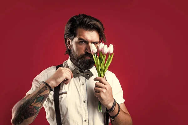 brutal bearded male with stylish look hold tulip bouquet, mothers day.