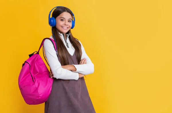 黄色の背景にスクールバックパック付きヘッドフォンで幸せな子供 — ストック写真