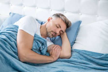 Olgun bir adam yatakta dinleniyor. Sabah erken saatlerde.