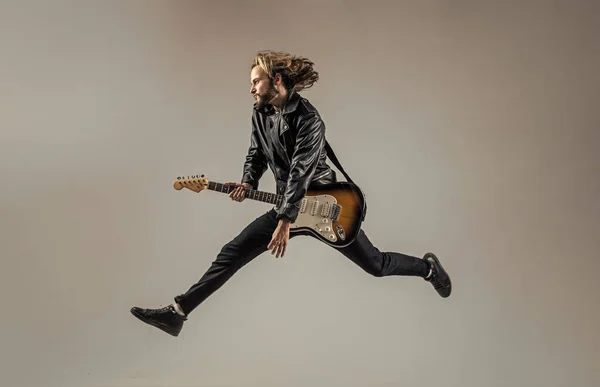 stylish crazy man. musical instrument. emotional bearded rocker in leather jacket. man long hair play electric guitar. rock music style. musician guitar player jumping. masterfully playing rock music.