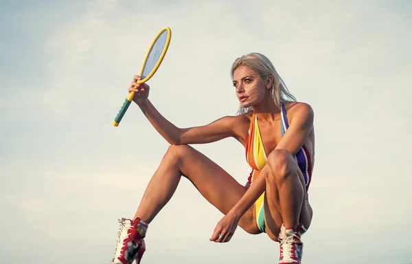 sexy woman with fit body in colorful rainbow swimsuit hold tennis racket on sky background, sport.