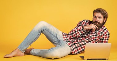 Kaba sakallı, kareli gömlek giyen, sakallı ve bıyıklı bir adam laptopta, işte çalışıyor..