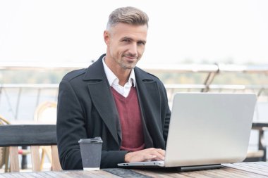 İnternette çalışan mutlu bir adam açık kafede kahve içiyor..