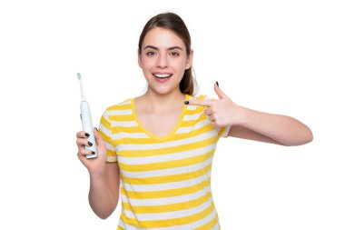 Neşeli genç kadın beyaz arka planda izole edilmiş elektrikli diş fırçasını işaret ediyor..