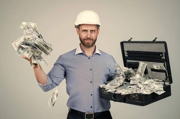 cheerful mature man businessman in building hard hat hold money case with dollar cash, income.