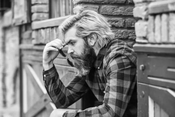 Depressed bearded man checkered shirt. Hipster dyed hair and beard. Hairdresser and barbershop. Brutal male with blond hair irish architecture background. Man casual fashion. Hipster in sunglasses.