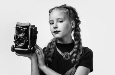 Fotoğraf stüdyosu. Geçmişi olan neşeli kız beyazda izole edilmiş görünüyor. Çocuk modası. Çocuk retro kamerayla fotoğraf çekiyor. Güzellik ve moda. Gazeteci ya da muhabir fotoğrafları. çocukluk mutluluğu.