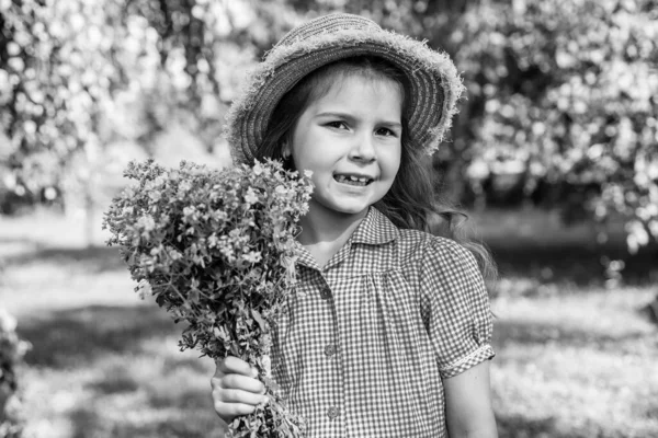 Small cute kid in sun hat and fashion dress holding summer flowers on natural landscape, mothers day.