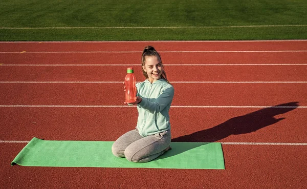 Drink water during fitness workout. Happy child show bottle sitting on yoga mat. Sport and hydration. Sports school. Physical education. While exercising continue to drink.