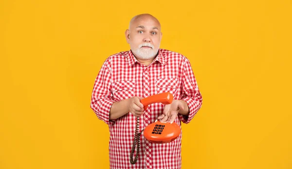 confused old man with vintage telephone on yellow background.