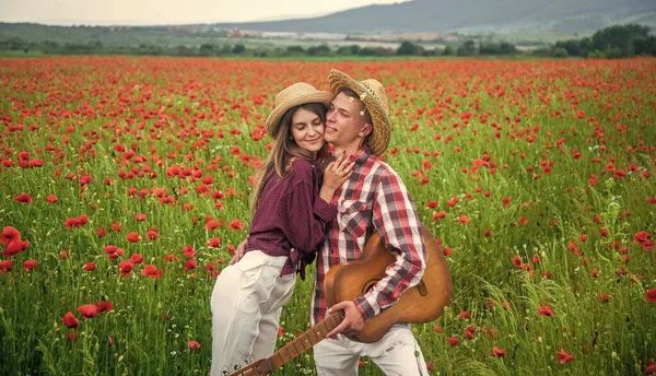 man and woman in poppy field. summer flower meadow. romantic couple among poppies. love and romance. opium. spring countryside. lovers with guitar in flower field. music. couple in love.
