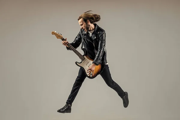 stylish crazy man. musical instrument. emotional bearded rocker in leather jacket. man long hair play electric guitar. rock music style. musician guitar player jumping. masterfully playing rock music.