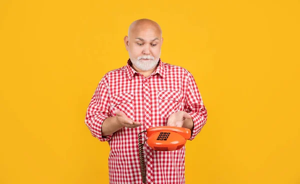 confused old man with retro telephone on yellow background.