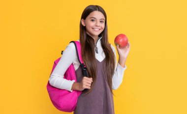 Sırt çantalı gülümseyen çocuk ve sarı arka planda elma..