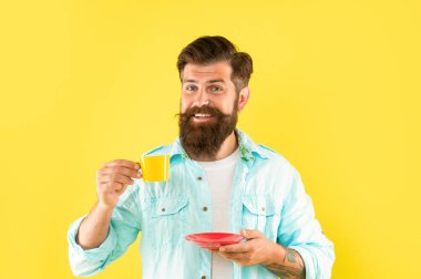 Gülümseyen olgun hippi sakallı, sarı arka planda kahve bardağı tutan, espresso içen.