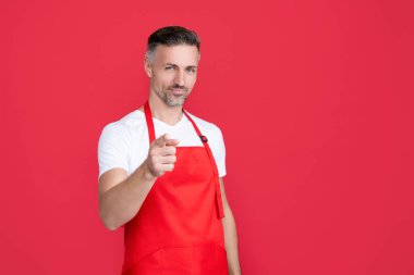 Kırmızı arka planda önlüklü olgun bir barmen. işaret parmağı.