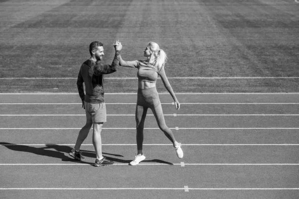 sport couple celebrate team win. fitness partners. athletic man and sexy woman compete in armwrestling. male and female coach on stadium running track arena. healthy lifestyle.