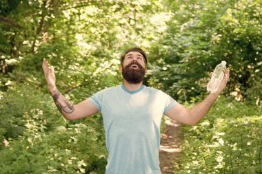 Yazlık elbiseli, sakallı mutlu sakallı adam ormanda su şişesi tutuyor, susuzluğunu gideriyor..