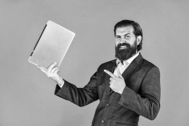 Bilgisayarlı mutlu beyaz sakallı hippi. Erkek çalışanın elinde finans raporu ve laptopta ortak çalışma alanı araştırmaları var. Modern iş dünyasındaki yeni teknoloji yalan söylüyor.