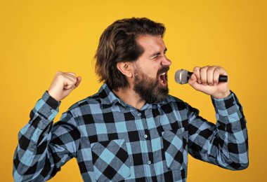 Kareli gömlekli vahşi adamın mikrofon ve karaokeyle uzun sakalı var..