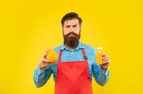 Σοβαρός Άνθρωπος Ποδιά Κρατώντας Πορτοκαλί Και Χυμό Μπουκάλι Κίτρινο Φόντο — Φωτογραφία Αρχείου