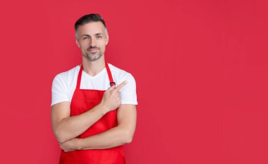 Kırmızı arka planda önlüklü olgun bir barista. işaret parmağı.
