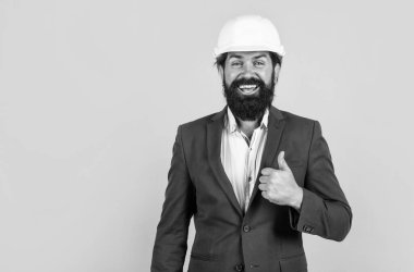 Miğferli mutlu bir mimar. Vahşi sakallı adam şantiyede çalışıyor. Proje üzerinde çalışıyorum. bina konsepti. Başlık takan mühendis ya da inşaatçı. Başparmağımı gösteriyorum. En iyi ve başarılı. Boşluğu kopyala.