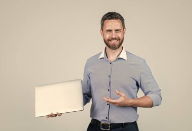 Tişörtlü, olgun, hırslı iş adamı sakallı, modern kablosuz dizüstü bilgisayarın, modern teknolojinin ürünlerini sunuyor..