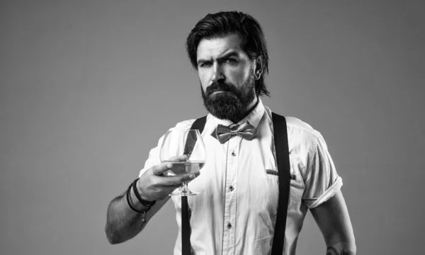 brandy or cognac. bearded man in suspenders drink scotch whiskey. brutal guy bartender wear bow tie. elegant male barman. handsome hipster drinking rum glass. party goer with alcohol.