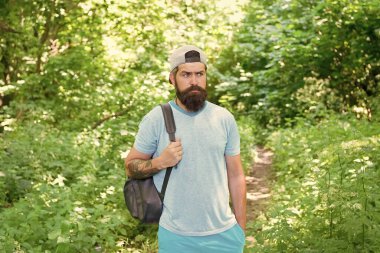 Sakallı ve bıyıklı, yaz tişörtlü ve şapkalı olgun sakallı adam ormanda sırt çantası tutuyor, sportif seyahat ediyor..
