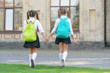 back view of two schoolgirls with school backpack walking together outdoor. childhood.