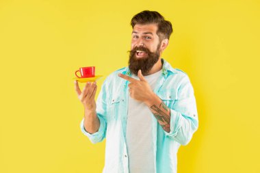 Tişörtlü, traşsız mutlu adam işaret parmağı sarı arka planda kahve, kahve fincanı.