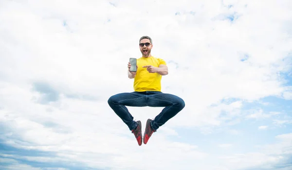 amazed man jumping and presenting smartphone on sky background.