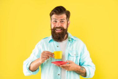Sarı arka planda kahve ve espresso ile gömlekli neşeli, tıraşsız bir adam..