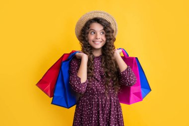 positive girl with curly hair hold shopping bags on yellow background.