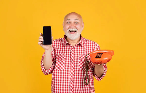glad old man with retro telephone and modern smartphone on yellow background.