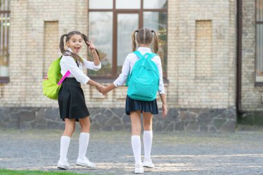 back view of two schoolgirls with school backpack walking together outdoor. back to school.