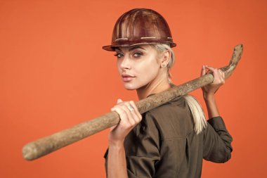 Daha derine in. Klimalı ve kasklı kadın. Kadın müteahhit kürek tutuyor. Bina ve inşaat. Bayan mimar. Turuncu arka planda mühendis. Ustabaşı kız güvenlik kaskı takıyor. İşçi Bayramı.