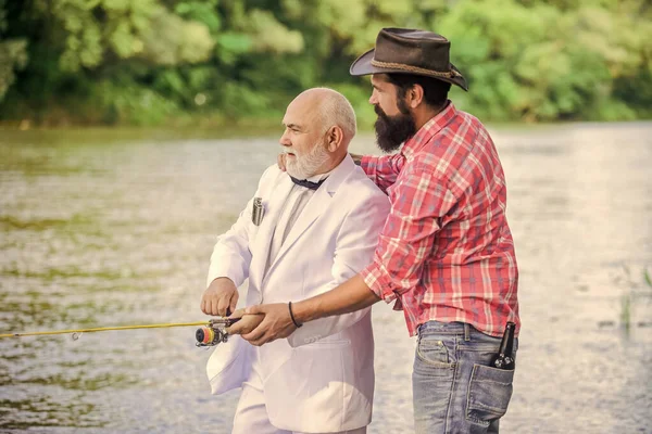 Learn to fish. Fishing skills. Men friends relaxing nature background. Personal instructor. Fish with companion who can offer help in emergency. Bearded man and elegant businessman fish together.