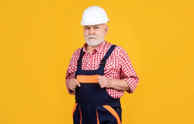 serious senior man builder in helmet on yellow background.