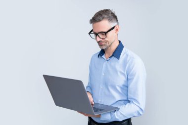 Gri arka planda bilgisayar üzerinde çalışan gözlüklü olgun işveren.