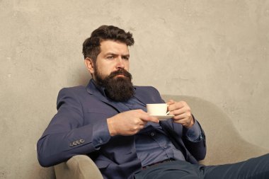 Sakallı adam dinlenme sırasında dinlenme koltuğunda çay ya da kahve içip rahatlıyor..