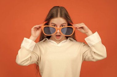 Parti gözlüklü hayret bir çocuk. Moda aksesuarı. Deliriyor. çocukluk mutluluğu. Şık bir parti havası. Turuncu arka planda gözlüklü neşeli çocuk. Eğlenceli genç kız eğleniyor..