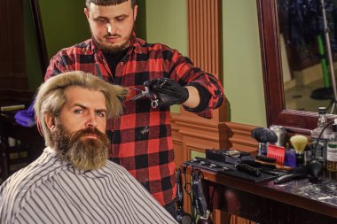 Seçiminden emin. Bıyıklı ve sakallı hippi. Adam yeni saç stili istiyor. Erkek güzellik ve moda. Berber dükkanında olgun bir adam. Kuafördeki vahşi sakallı adam. Erkek müşteriyle berber..