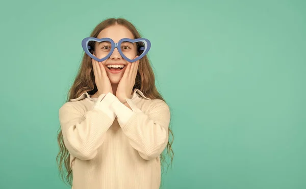 fancy party look. happy funny kid in glamour eyeglasses on blue background. funky teen girl having fun. glad child in party glasses. fashion accessory. going crazy. childhood happiness.